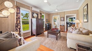 A spacious living room with a sofa, armchair, and a coffee table. A kitchen area is visible in the background. - Umetsu, Hanalei's Timeless Charm w/ AC TVNC#5096 (Hanalei)