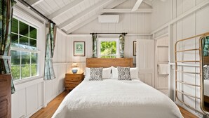 A bedroom with a wooden headboard, a bed with white bedding, a nightstand with a lamp, a window with curtains, and a ceiling fan. - Palaka Cottage, A Timeless Hanalei Stay TVNC#1091 (Hanalei)