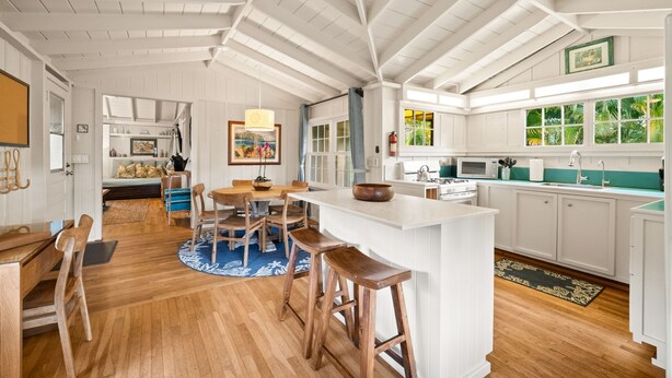 A spacious kitchen with a large island, wooden flooring, and white cabinetry. - Palaka Cottage, A Timeless Hanalei Stay TVNC#1091 (Hanalei)