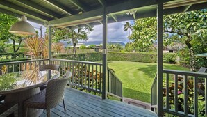 A covered outdoor area with a table and chairs, a hanging light fixture, and a view of a well-maintained lawn and trees. - Palaka Cottage, A Timeless Hanalei Stay TVNC#1091 (Hanalei)
