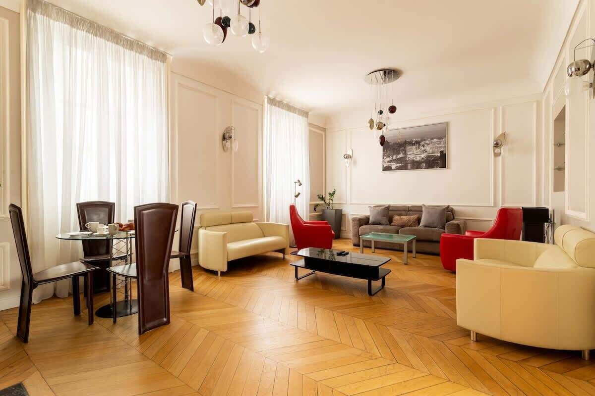 Ein geräumiges Wohnzimmer mit Holzparkett, einem Essbereich mit rundem Tisch und Stühlen sowie einer Sitzecke mit Sofas und Sesseln.