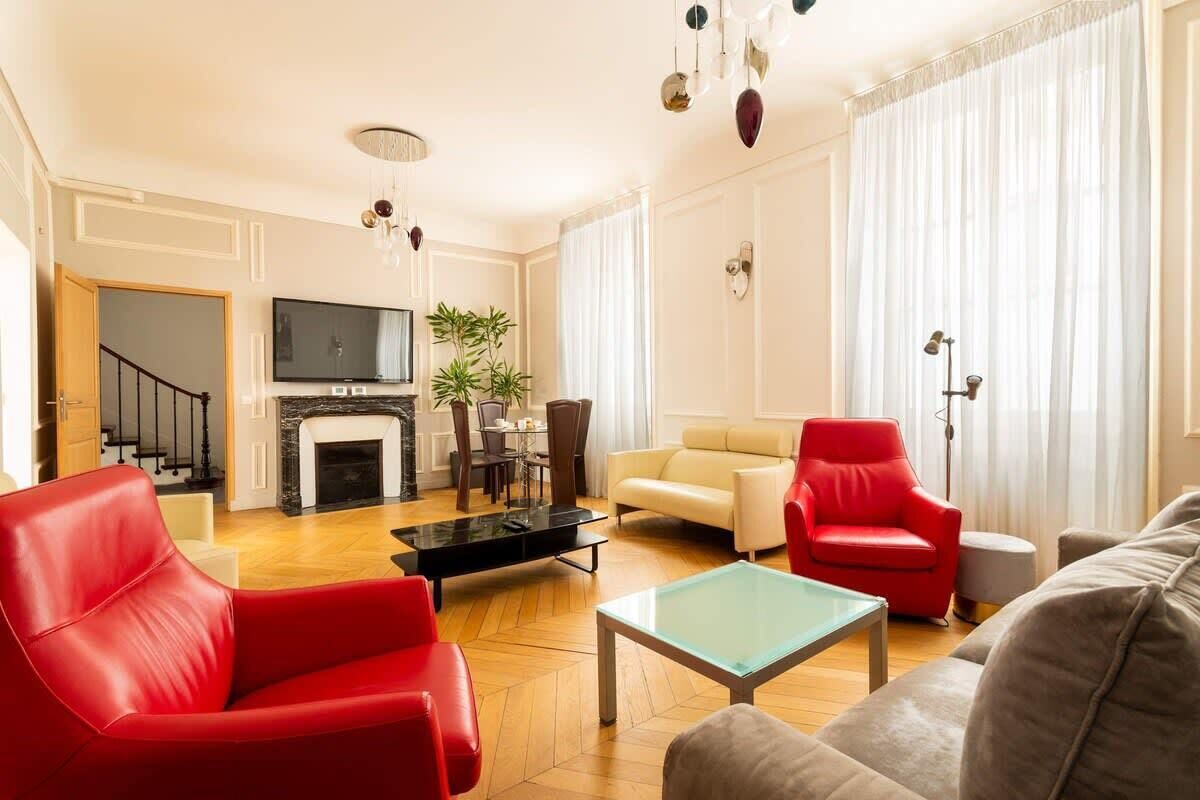 Uma sala de estar com lareira, televisão, uma poltrona vermelha, sofá bege e mesa de centro de vidro.
