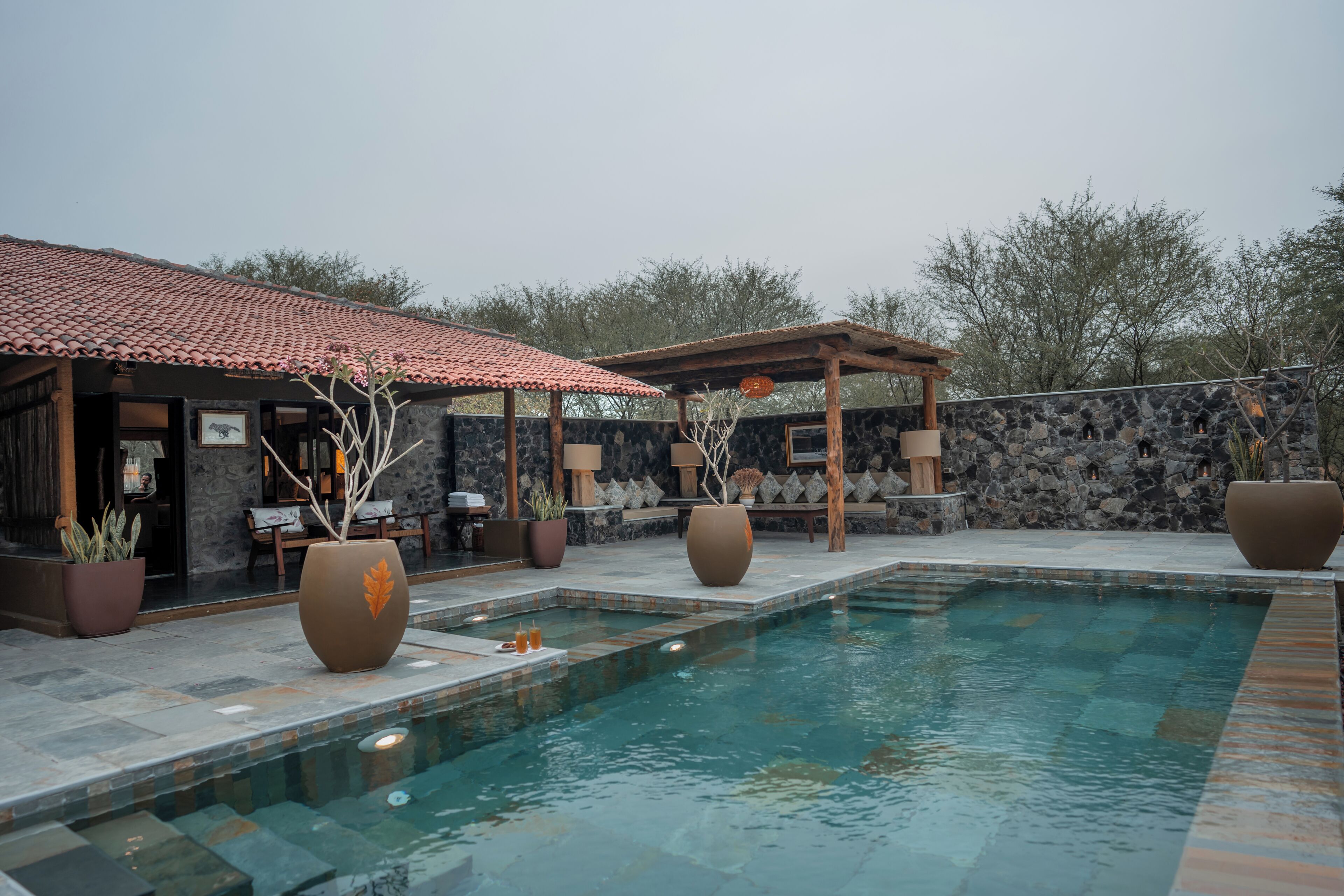 A pool area with a stone wall, wooden pergola, and lounge seating.