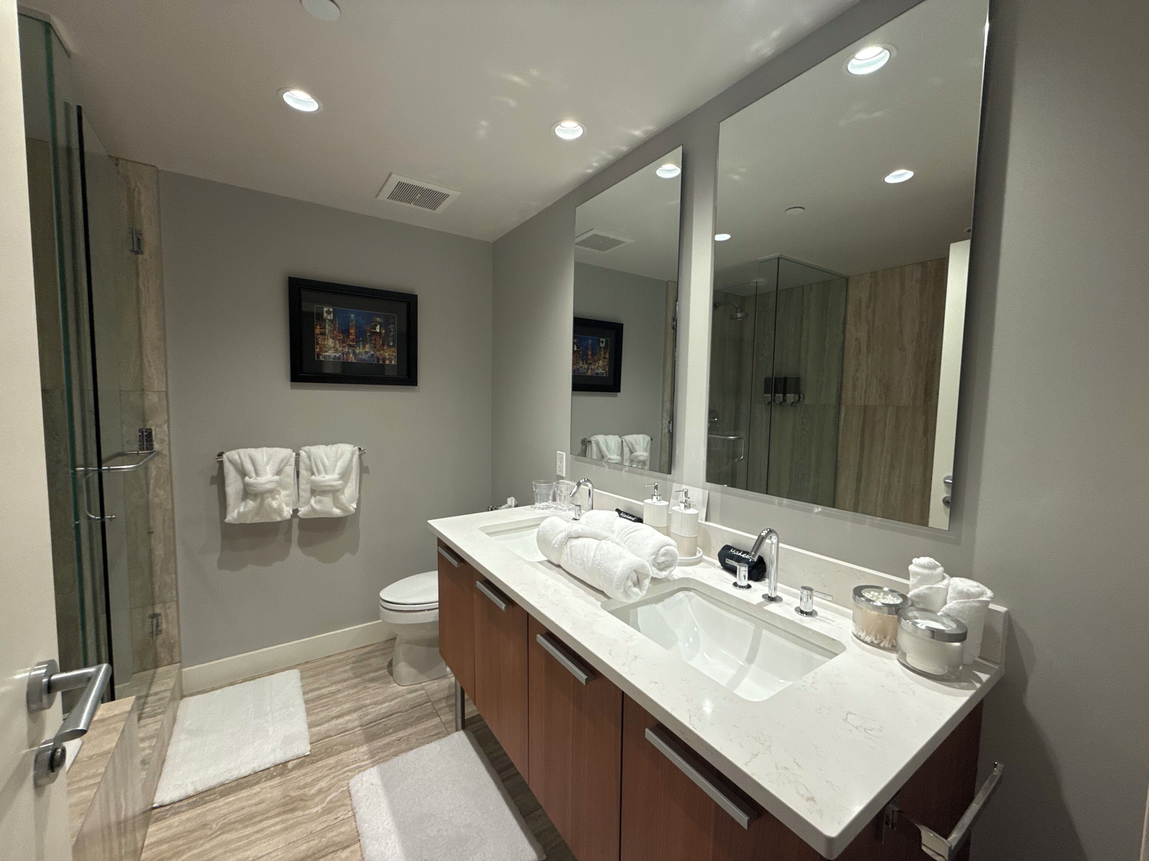 Un baño moderno con un espejo grande, dos lavamanos, una ducha y un inodoro.