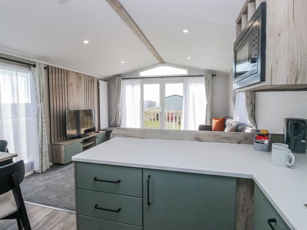 A modern kitchen with a built-in microwave, a TV, and a large window overlooking a deck. - Sand Martin (St Bees)