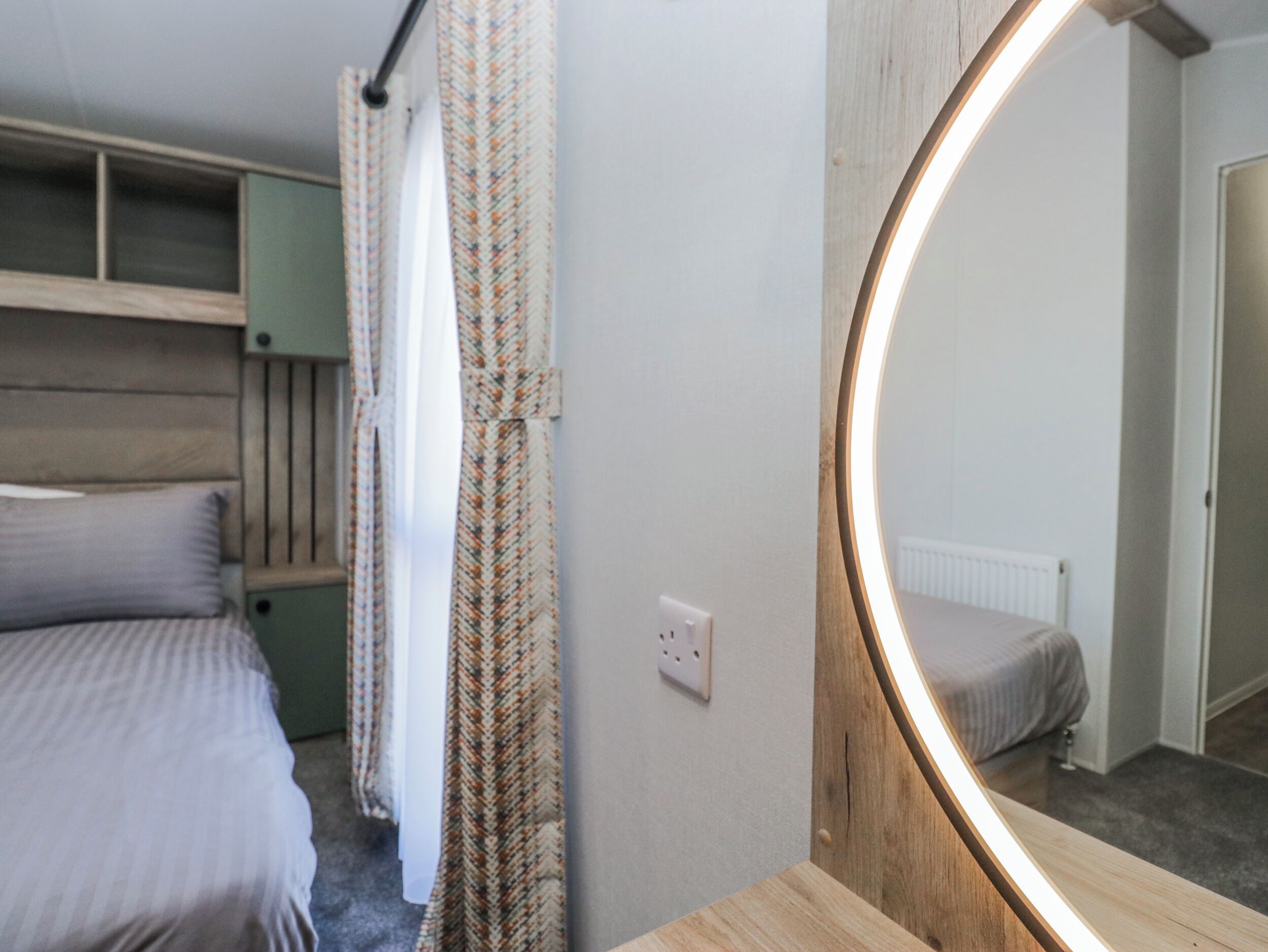 Een slaapkamer met een bed, een spiegel, een radiator en een raam met gordijnen.