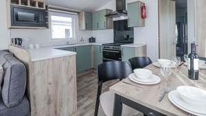 A compact kitchen with a microwave, stove, and sink, a dining table with chairs, and a fire extinguisher. - Sand Martin (St Bees)
