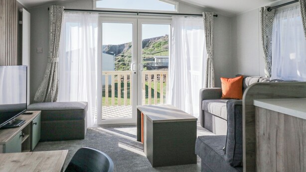 A modern room with a balcony, a sofa, a table, and a TV. - Sand Martin (St Bees)