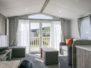 A modern room with a balcony, a sofa, a table, and a TV. - Sand Martin (St Bees)