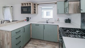 A compact kitchen with a microwave, stove, sink, and wooden cabinets. - Sand Martin (St Bees)