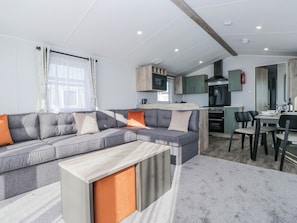 A modern living room with a grey sectional sofa, a wooden coffee table, and a kitchen area with green cabinets and a stove. - Sand Martin (St Bees)