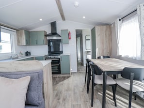 A compact kitchen with a stove, oven, and a small dining area with a table and chairs. - Sand Martin (St Bees)
