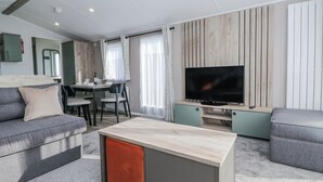 A modern living room with a sofa, a coffee table, a TV, and a dining area. - Sand Martin (St Bees)