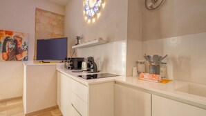 Eine moderne Küche mit Einbauherd, Kaffeemaschine und Mikrowelle. Über dem Herd befindet sich ein kleines Regal und auf der Arbeitsfläche eine Reihe von Küchenutensilien.
