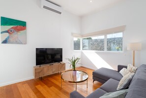 Ein modernes Wohnzimmer mit Fernseher, einer Couch, einem Couchtisch und einem Gemälde an der Wand.