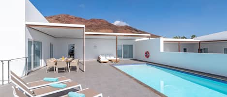 A poolside area with sun loungers, a table with chairs, and a lifebuoy on the wall.