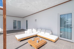 Ein moderner Außenbereich mit einer Eckcouch, einem Holztisch und einer Glastür zum Pool.