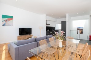 Ein modernes Wohnzimmer mit einer Couch, einem Glastisch, Korbstühlen, einem Flachbildfernseher und Kunstwerken an der Wand.