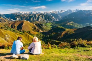 Two people sitting on a grassy hill overlooking a mountainous landscape.