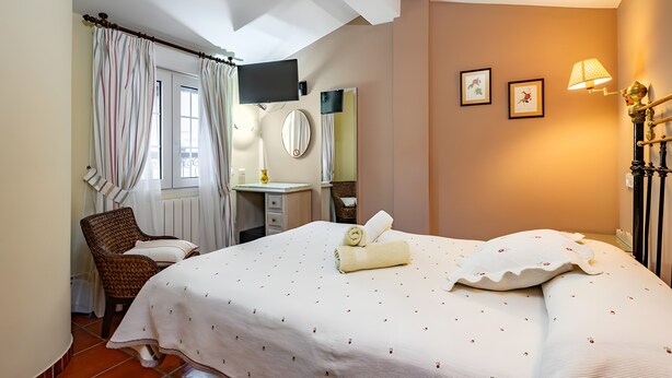 Un dormitorio con cama, una silla, escritorio, espejo y lámpara.
