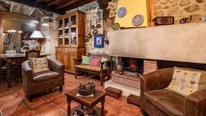 A rustic interior with a stone wall, wooden furniture, a fireplace, and a tiled floor.