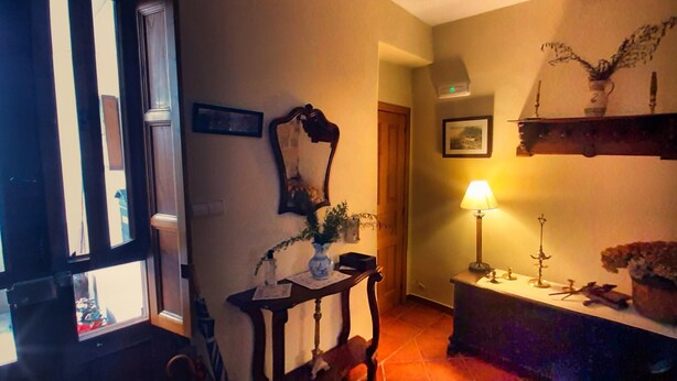 Een kamer met een houten deur, een spiegel, een tafel met een vaas, een lamp en een plank met decoratieve objecten.
