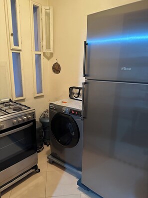 A compact kitchen with a gas stove, oven, washing machine, and a stainless steel refrigerator. - Cosy room - Chez Redouan 5 minutes from Souk Alhad (Agadir)