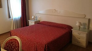 Una camera da letto con un letto, due comodini, una sedia, una finestra con tende e un termosifone.