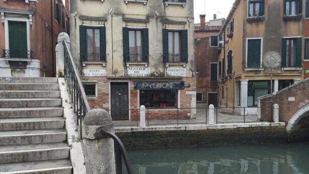 Un edificio lungo un canale con un cartello che riporta 'L'GRIFONE' e una scala che conduce a una porta.