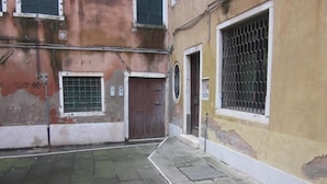 Un vialetto stretto con pavimento in piastrelle, una porta marrone e una finestra con inferriate.