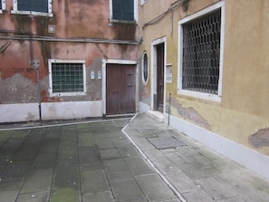 A narrow alleyway with a tiled pavement, a brown door, and a window with bars. - 2 rooms apart Venice resorts 1 near bus and train (Venezia)