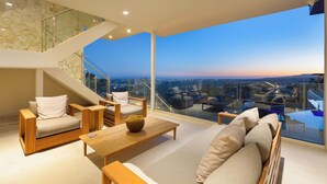 Ein modernes Wohnzimmer mit hoher Decke, einer Treppe und einem großen Panoramafenster mit Blick auf die Stadt.