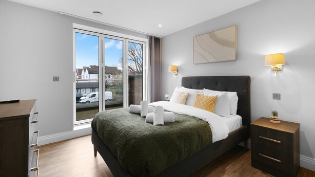 A modern bedroom with a large bed, bedside lamps, a view through a sliding door, and a wooden dresser. - The Isleworth 2BR 2BA with Gated Parking & Balcony (Isleworth)