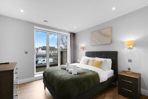 Een moderne slaapkamer met een groot bed, nachtlampjes, uitzicht door een schuifdeur en een houten dressoir.