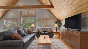 Un loft spazioso con soffitto alto, ampie finestre, un divano in pelle, un tavolino da caffè in legno e una TV su un mobile in legno.