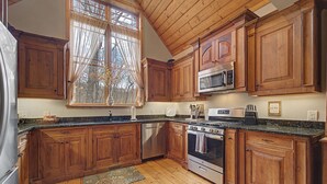 Una cucina con mobili in legno, frigorifero in acciaio inox, lavastoviglie, forno a microonde, forno e lavello.