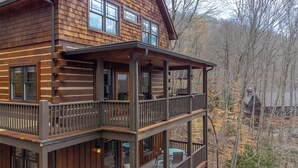 Una baita di legno a due piani con un balcone e un'area salotto esterna.