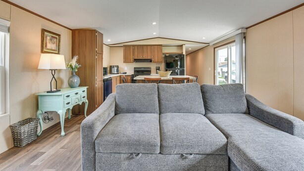 A modern living room with a grey sofa, wooden cabinets, a small table with a lamp, and a view of the kitchen in the background. - 2 Mi to Ocean! Family-friendly Emerald Coast Haven (Fort Walton Beach)