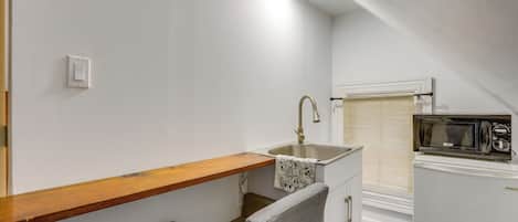 A small kitchenette with a wooden shelf, a sink, a chair, and a microwave.