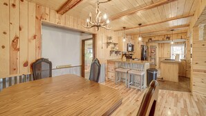A wooden interior with a dining table, chairs, a chandelier, and a kitchen area. - Private Beach & Fishing Pond! Eufaula Family Cabin (Eufaula)