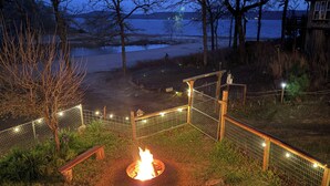 A fire pit surrounded by a wooden fence, a bench, and a view of a lake at dusk. - Private Beach & Fishing Pond! Eufaula Family Cabin (Eufaula)