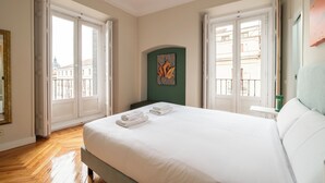 Une chambre d’hôtel avec un grand lit, deux fenêtres, un mur d’accent vert et une vue sur la ville.