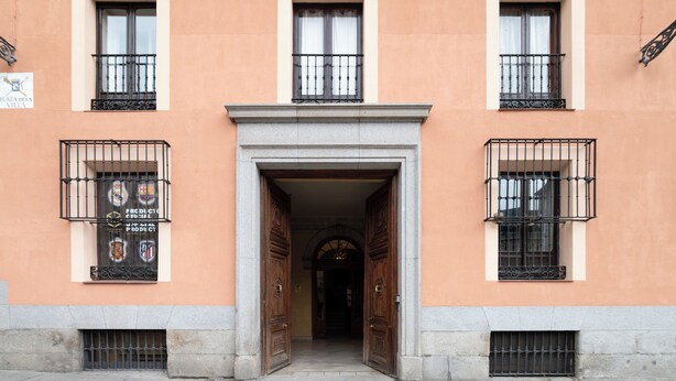Un bâtiment doté de trois fenêtres, chacune ornée d’un balcon en fer forgé noir. On y trouve deux grandes portes en bois, situées au centre.