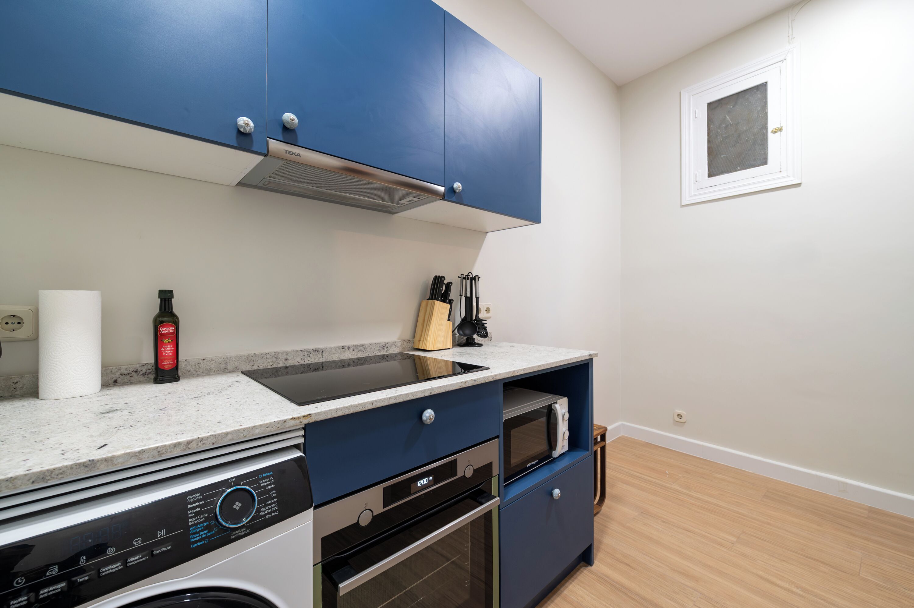 Cocina compacta con armarios azules, un microondas integrado y una lavadora.