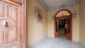 Un couloir avec une porte en bois, un sol carrelé et une porte en arc donnant sur un escalier.