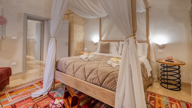 A four-poster bed with a canopy, a small round table with a lamp, a colorful rug, and a red chair. - Antony Suite Strada Apartment with Wi-Fi and Air Conditioning (Lecce)