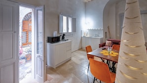 A modern kitchen with white cabinets, a microwave, and a dining area with orange chairs and a wooden table. - Antony Suite Strada Apartment with Wi-Fi and Air Conditioning (Lecce)