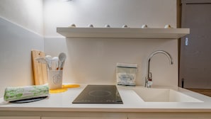 A kitchen with a white countertop, a built-in induction cooktop, a sink, and a stainless steel faucet. - Antony Suite Strada Apartment with Wi-Fi and Air Conditioning (Lecce)