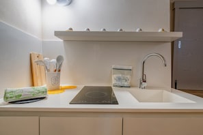A kitchen with a white countertop, a built-in induction cooktop, a sink, and a stainless steel faucet. - Antony Suite Strada Apartment with Wi-Fi and Air Conditioning (Lecce)