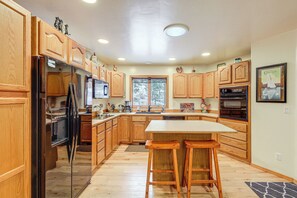 A kitchen with wooden cabinets, a refrigerator, a microwave, a sink, and a large island with bar stools. - Deck + Game Room: Secluded Cabin Near Lake Cascade (Cascade)